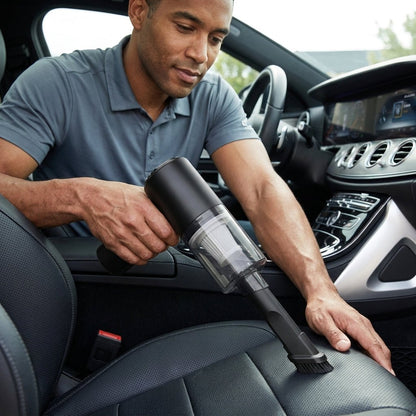 Hombre usando el aspirador inalámbrico negro para limpiar el asiento de su coche